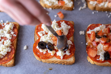 Young female chef in kitchen at home preparing mozzarella salami tomato and olives sandwiches. Healthy eating