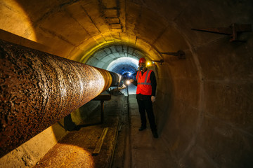 Tunnel worker examines pipeline in underground tunnel