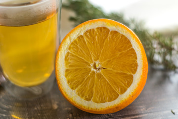 Vitamin lemon yellow tangerine peel drink in a transparent glass. Cinnamon and sliced orange on a wooden table. Juniper sprig