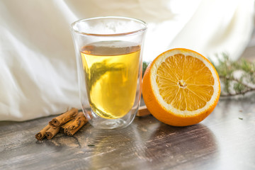 Vitamin lemon yellow tangerine peel drink in a transparent glass. Cinnamon and sliced orange on a wooden table. Juniper sprig