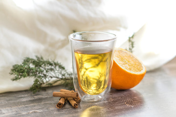 Vitamin lemon yellow tangerine peel drink in a transparent glass. Cinnamon and sliced orange on a wooden table. Juniper sprig