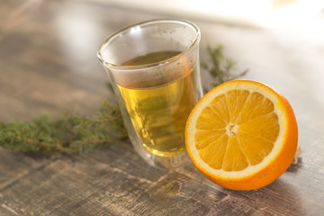 yellow tangerine peel drink in a transparent glass. Sliced orange on a wooden table. Juniper sprig