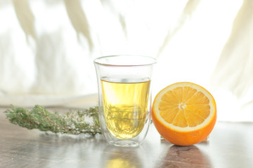 yellow tangerine peel drink in a transparent glass. Sliced orange on a wooden table. Juniper sprig