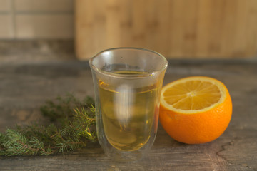 yellow tangerine peel drink in a transparent glass. Sliced orange on a wooden table. Juniper sprig