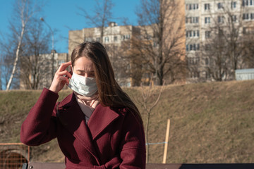 girl is sitting on a bench in the park. puts on a face a white protective medical mask. protection...