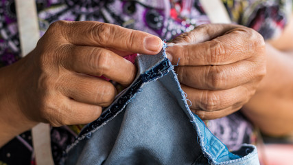 Hands and fingers of elderly women repairing denim.