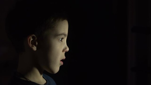 A boy is standing in the dark. Side view. Not expressive face. Without emotion. Close-up. Education.