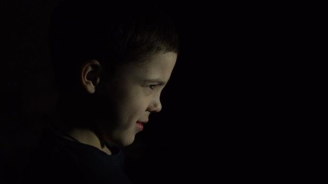 A boy is standing in the dark. Side view. Offended face. Close-up. Punishment. Learning problems.