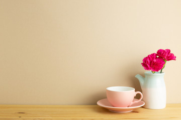 Coffee cup with spray carnation flower in vase on wooden table with brown background. Floral arrangement, copy space