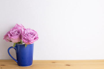 Purple rose flowers in ceramic cup on wooden table with white background. Spring floral arrangement, copy space