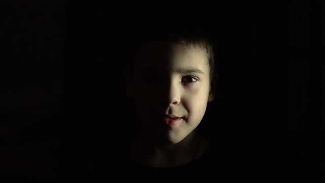A boy is standing in the dark. Flashing light source. Close-up.