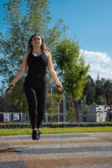 Mujer joven fitness con ropa oscura brinca la cuerda durante un día  verde soleado 