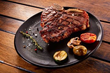 Grilled beef steak with rosemary, salt and pepper on black stone plate. Grilled striploin sliced steak. Juicy thick grilled beef steak seasoned with rosemary fresh of the summer BBQ.