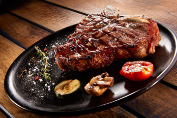 Grilled beef steak with rosemary, salt and pepper on black stone plate. Grilled striploin sliced steak. Juicy thick grilled beef steak seasoned with rosemary fresh of the summer BBQ.