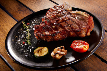 Grilled beef steak with rosemary, salt and pepper on black stone plate. Grilled striploin sliced steak. Juicy thick grilled beef steak seasoned with rosemary fresh of the summer BBQ.