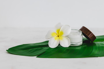 Fototapeta na wymiar vegan natural beauty, pot of face cream on tropical green leaf with monoi flowers