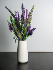 Simple white ceramic vase filled with purple flowers sitting on a black slate background with a white background.