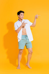 Full body of young handsome Asian man in casual summer outfit pointing two hands aside on colorful yellow background