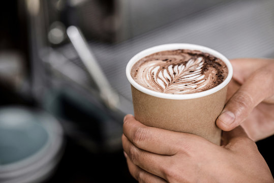Close up shot of male hands holding take away cup of brewed hot coffee with Fern latte art design