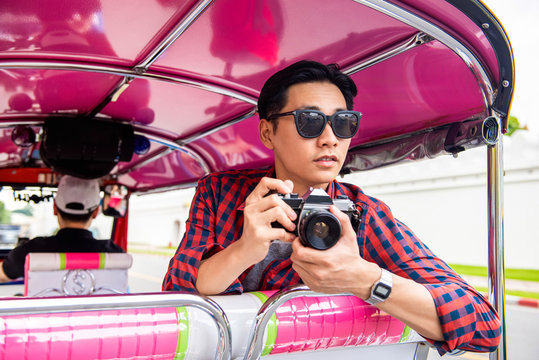 Handsome male Asian tourist holding camera on tuk tuk taxi in Bangkok Thailand during summer vacation solo traveling