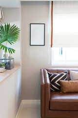 Brown leather sofa with graphic pattern pillow in elegant living room interior by the window. Modern stylish interior.