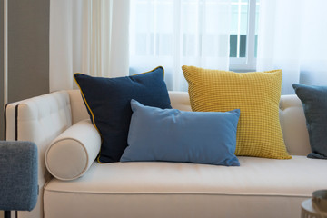 Interior of minimalistic living room with white sofa and yellow, blue cushion.