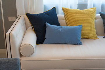 Interior of minimalistic living room with white sofa and yellow, blue cushion.