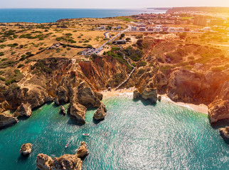View of stunning turquoise beach, hotel, houses and a wooden stairs on top of golden color rock, Algarve, Portugal. 