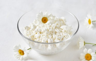 Homemade cottage cheese and cream in glassware. on a white background. Soft focus. Chamomile flowers as a symbol of rustic.  Copy Space