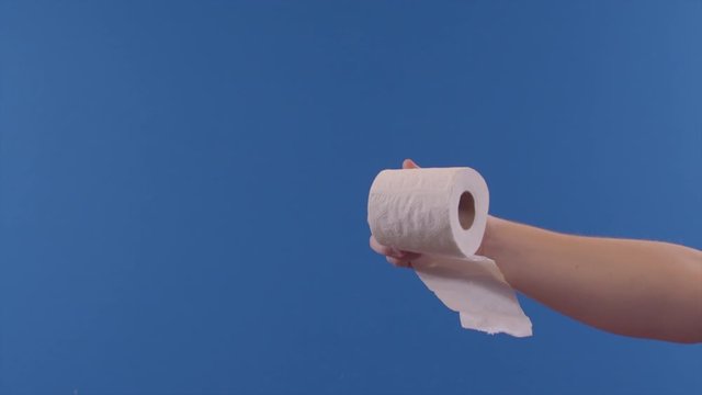 A person is holding out a toilet paper roll in front of a blue screen.