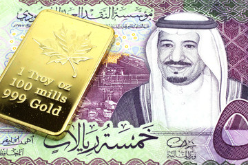 A macro image of a colorful riyal Saudi Arabian note with a Canadian one ounce gold ingot close up