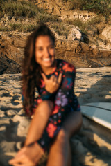 Background vintage out of focus Surfer girl with white surfboard seating on the beach with shaka sign in sunset.