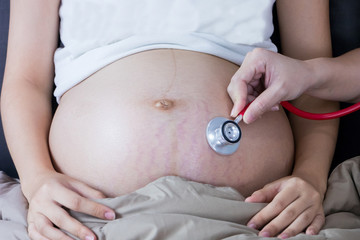 Portrait of Beautiful young pregnant women using stethoscope listening to her tummy.Pregnancy health care preparing for baby concept.Motherhood among teenage mother.