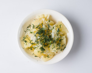 Boiled potatoes with dill in a white bowl on a light background. View from above