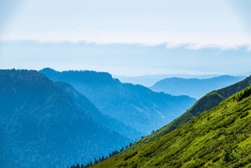 Green mountain slope. Layers of mountains in the haze during sunset. Krasnaya Polyana, Sochi, Caucasus, Russia.