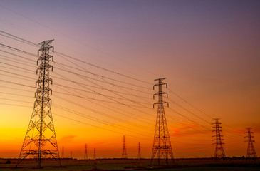 High voltage electric pylon and electrical wire with sunset sky. Electricity poles. Power and energy concept. High voltage grid tower with wire cable at rice farm field near industrial factory.