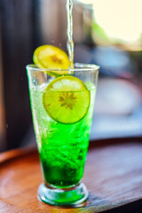 Iced green soda with lemon in glass on wood table.