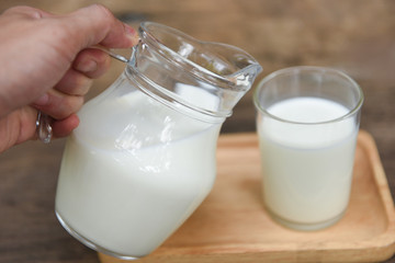 Fresh milk natural in a glass jug and  Pouring milk into glass on wooden background