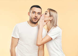 Young woman whispering secrets to man over beige background