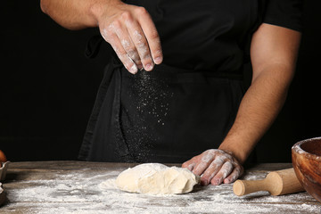 Man sprinkling dough with flour in kitchen