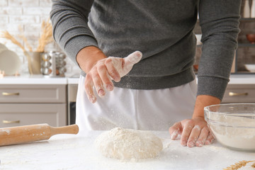 Man sprinkling dough with flour in kitchen