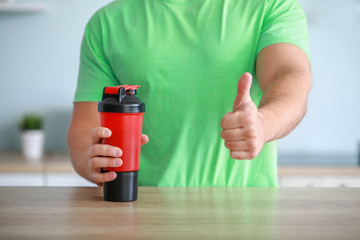Sporty man with protein shake showing thumb-up in kitchen, closeup
