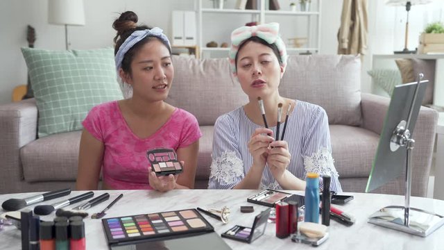Two young asian korean girls making video for blog on cosmetic face camera. charming lady online influencer showing make up brushes and recording beauty tutor video. woman teach audience doing makeup
