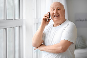 Portrait of elderly man talking by phone near window