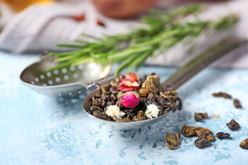 Strainer with dry tea leaves on color background