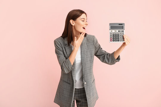 Surprised young woman with calculator on color background