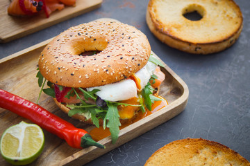 Bagel with salmon and poached egg on wooden board, Dark background, Breakfast bun