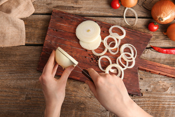 Woman cutting fresh raw onion on wooden table