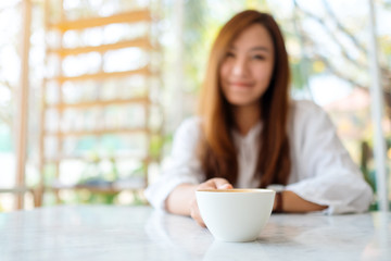 Closeup image of a woman holding a cup of hot coffee on the table