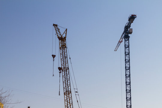 Two construction cranes on the blue sky background. Backlit images.